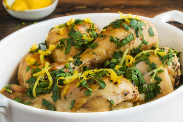 Baked chicken legs with fresh parsley and lemon juice and zest in white casserole on wooden rustic...