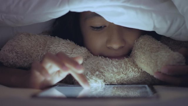 Little girl using tablet in the bedroom.