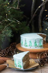 Celebratory cake decorated with painted Christmas trees on a dark background of branches and cones. Rustic style.