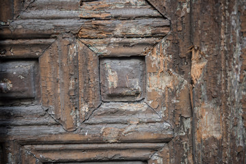 Closeup of a locked and closed wooden door is seen on this picture. The design on the door can be seen clearly. It seems the brown colored door is old.