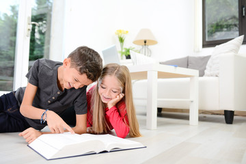 two young happy kids brother and sister together having fun at home reading encyclopedia book