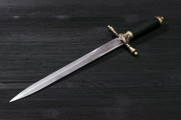 Dagger knife isolated on the black wooden background.
