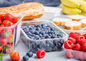 Plastic tray containers of fresh organic healthy beries and bread for fruit sandwiches. Blueberries, strawberries, bananas and raspberries on stone kitchen table background.