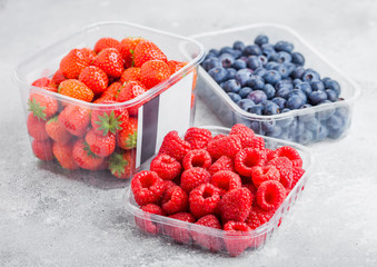 Plastic tray container of fresh organic healthy blueberries, strawberries and raspberries on stone kitchen background.
