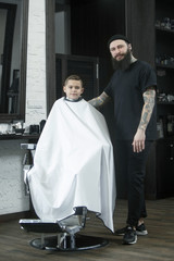 Children hairdresser cutting little boy against a dark background. Contented cute preschooler boy getting the haircut.