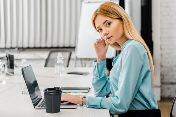 side view of attractive businesswoman at workplace with laptop and coffee to go in office