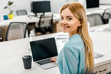 smiling businesswoman at workplace with laptop and coffee to go in office