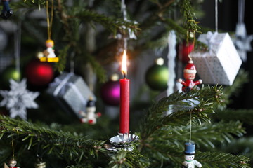 Weihnachtsbaum mit brennender roter Kerze, traditionellem Christbaumschmuck, Holzfigen, Geschenken, Weihnachtskugeln, Stern, Weihnachtsmann, Engel