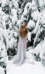 Junge Frau mit langen Haaren im Winter, mit langem weißen Kleid im Schnee Eis friert im Winter  schaut nach oben und wärmt sich mit ihren Armen 