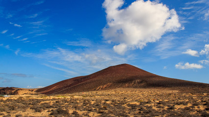 Fototapeta na wymiar Volcanic mountain on a sunny summer day under an intense blue sky with fluffy white clouds. Scenery on La Graciosa Island, Canary, Spain.