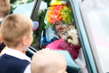 The clown looks through the glass of the car for joyful children