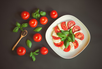 Tomatoes, green basil, pepper and plate of caprese salad  on dark background. Top view.