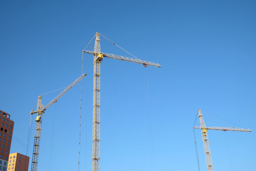 Big yellow construction tower cranes on dwelling construction over blue sky