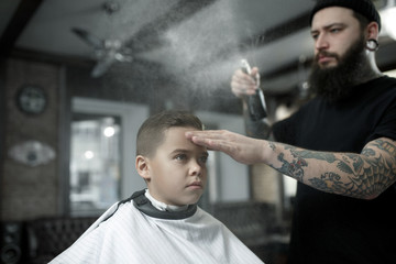 Children hairdresser cutting little boy against a dark background. Contented cute preschooler boy getting the haircut.