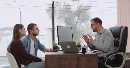 Attractive young couple have a meeting with a bank manager or realtor to make a deal to get a mortgage for a house they have a look through the laptop , office man explain the condition and they - Powered by Adobe