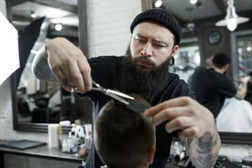 Children hairdresser cutting little boy against a dark background. Contented cute preschooler boy getting the haircut.