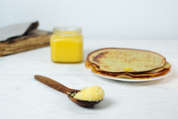 Pancakes roasted on a tray are plentifully covered with butter and a wooden spoon with butter