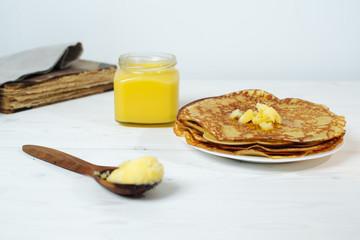 Pancakes roasted on a tray are plentifully covered with butter and a wooden spoon with butter