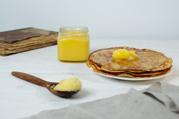 Pancakes roasted on a tray are plentifully covered with butter and a wooden spoon with butter