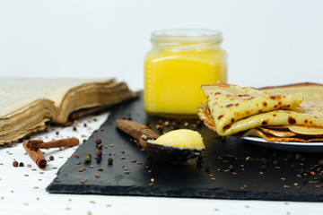 Pancakes roasted on a tray are plentifully covered with butter and a wooden spoon with butter