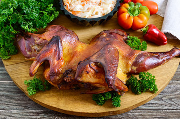 Whole baked flattened chicken with a golden crispy crust with fresh vegetables, herbs and cabbage salad on a wooden tray. 