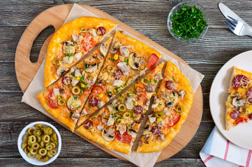 Tasty pizza with mushrooms, chicken, pepperoni, olives, corn cut into pieces on a wooden tray. The top view