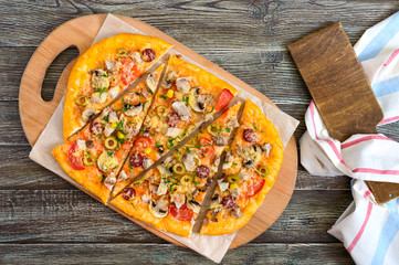 Tasty pizza with mushrooms, chicken, pepperoni, olives, corn cut into pieces on a wooden tray. The top view