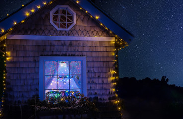 Fairy-tale house in the lights and a luminous window with a Christmas tree and a starry sky. Night...