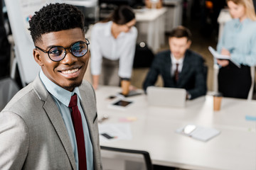 selective focus of smiling african american businessman and colleagues behind at workplace in office