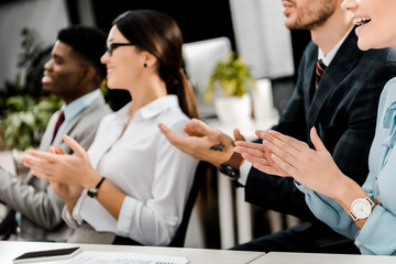 partial view of multiracial businesspeople applauding to speaker in office