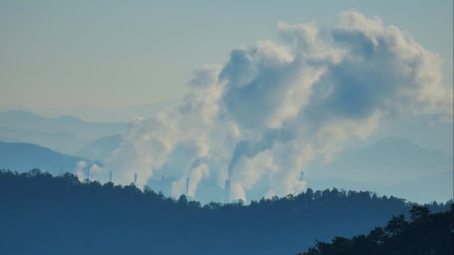The atmosphere is tainted by air pollution as smoke and smog envelop the landscape, emanating from industrial activities, particularly a coal power plant in the morning mist