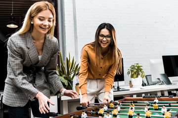 happy businesswomen playing table football together in office
