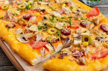 Tasty pizza with mushrooms, chicken, pepperoni, olives, corn cut into pieces. Close up