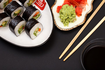 Sushi rolls in nori seaweed sheets and pickled ginger and wasabi on plates.