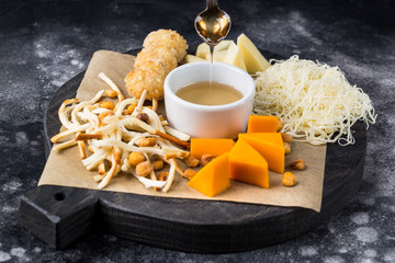 Wooden round board with tasty cheese on black background with honey