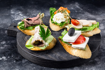 Different delicious toasts with vegetables meat and cheese on dark background round board
