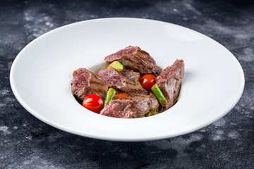 Sliced medium rare grilled Beef steak Ribeye with grilled onions and cherry tomatoes on plate on dark background