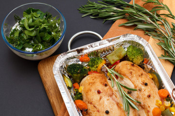 Baked chicken breasts or fillet in metal container with vegetables on cutting board.