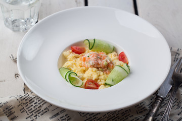 Omelette stuffed with salted salmon on a white plate on wooden white background.