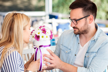 Young man giving beautiful flower bouquet to his girlfriend for birthday or anniversary. Romantic moments in a cafe