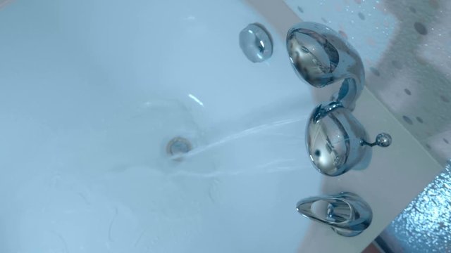 A beautiful faucet with a shower head is built into the corner of the bath, a hand presses the handle and water starts to flow from the tap in to the bath. Top view. Macro. Closeup