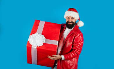 Happy man in Santa Claus hat with big gift. Santa man hold christmas gift on hand. Christmas, new year, winter holiday celebration. Christmas mood. Bearded man in Santa hat with big Christmas gift box
