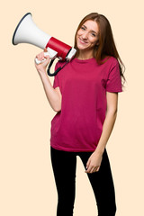 Young redhead girl holding a megaphone on isolated yellow background