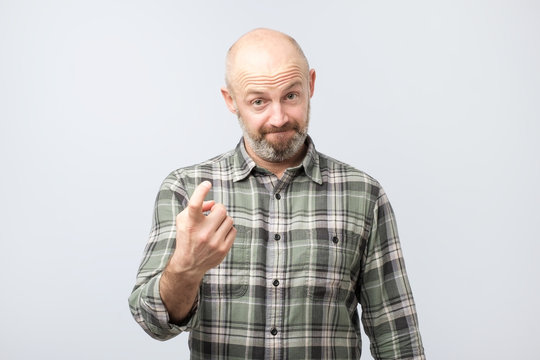Playful bearded adult showing come here gesture with index finger and smiling over gray background.