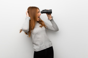 Redhead girl over white wall and looking in the distance with binoculars