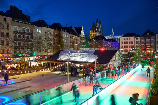 Weihnachtsmarkt in Köln am Heumarkt bei Nacht. Sicht auf die Eisbahn auf der Besucher Schlittschuh laufen können.