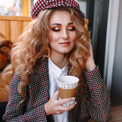 Autumn luxury look, pretty cool smiling young woman with coffee cup using smartphone walking in...