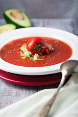 Cold summer tomato dish. Gaspacho soup with toast, cherry tomatoes, pepper, basil herbs, avocado