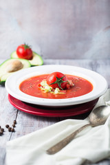 Cold summer tomato dish. Gaspacho soup with toast, cherry tomatoes, pepper, basil herbs, avocado