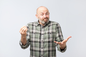 Mature european man explaining something simple being questioned someone, frowning and grimacing with clueless expression over gray wall